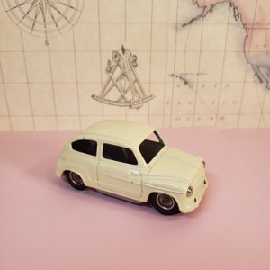 May include: A white toy car with black wheels. The car is a vintage model and has a classic design.