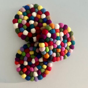 May include: Three colourful felt coasters made of small, round balls of wool in various shades of red, blue, green, yellow, pink, purple, and white.