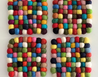 May include: Set of four colorful felt coasters. Each coaster is made of a grid of small, colorful felt balls. The coasters are perfect for protecting surfaces from heat and scratches.