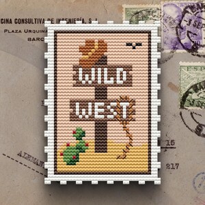 Puede incluir: Un diseño de punto de cruz que se asemeja a un sello postal, con un poste indicador con el texto "WILD WEST". El diseño incluye un cactus, un sombrero de vaquero y una serpiente, todo en tonos tierra. El sello tiene un borde blanco perforado.