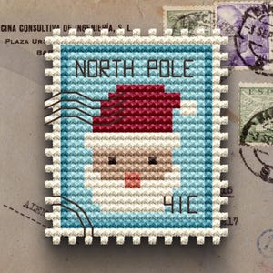 May include: A cross-stitch design of a postage stamp featuring Santa Claus with the text "NORTH POLE" and "41C". The stamp has a light blue border and a red Santa hat. The background includes other stamps and aged paper.