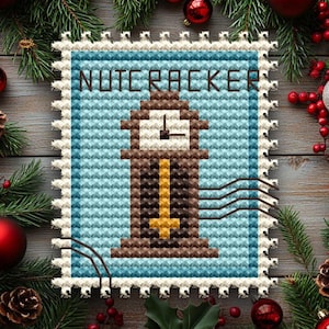 Könnte beinhalten: Ein Kreuzstich-Design mit einem Uhrturm und dem Wort "NUTCRACKER" darüber. Der Uhrturm ist braun und goldfarben, vor einem hellblauen Hintergrund. Das Design ist von einem weißen, gezackten Rand umgeben, der einer Briefmarke ähnelt. Festliche Weihnachtsdekorationen umgeben das Design.
