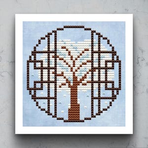 Könnte beinhalten: Kreuzstich-Kunstwerk eines Baumes im Winter, umgeben von einem braunen geometrischen Rahmen. Der Baum hat einen braunen Stamm und Äste, mit weißen und hellblauen Details, die Schnee darstellen. Der Hintergrund ist hellblau.