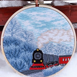 May include: A cross-stitch embroidery hoop depicting a red and black train engine with white smoke billowing from the chimney, set against a blue and white wintery background.