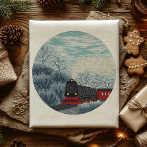 Puede incluir: Una obra de arte de punto de cruz de una escena invernal con un tren de vapor negro y rojo que viaja por un bosque nevado. La obra de arte es circular y está colocada sobre un lienzo de color claro. La imagen está rodeada de decoraciones navideñas.