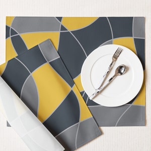 May include: Two placemats with a geometric pattern in grey and yellow, with a white plate and cutlery on top.