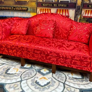 Pode incluir: Um sofá vermelho com um padrão floral e três almofadas a condizer. O sofá tem encosto curvo e pernas de madeira. O sofá está colocado sobre um tapete estampado.