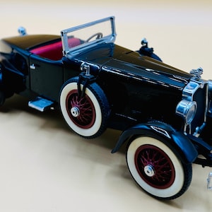 May include: A black vintage car model with a white windshield and red wheels. The car has a chrome grill and headlights.