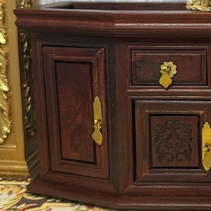 May include: A dark wood jewelry box with two doors and three drawers. The box has gold-colored handles and a carved design on the front.