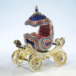 May include: A decorative miniature carriage figurine crafted with a gold-tone metal frame, featuring a deep blue and red enamel finish. The carriage is adorned with small, sparkling red and clear crystals along the edges and wheels.