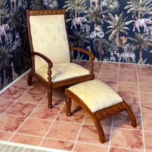 May include: Miniature wooden armchair and footstool set. The chair has a high back and armrests, with a cream-colored diamond-patterned cushion. The footstool mirrors the chair's design. The set is made of dark wood.