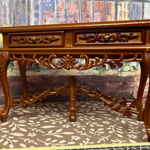May include: A wooden console table with two drawers and intricate carvings. The table has a dark brown finish and ornate legs.