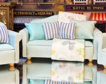 May include: A set of three light blue upholstered furniture pieces, including a sofa and two armchairs. The sofa has a floral patterned throw blanket and striped pillows. The armchairs have striped pillows.