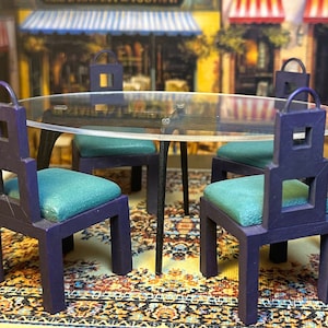 May include: A miniature dining set with a glass top table and four chairs. The chairs are dark purple with teal cushions and a geometric design. The set is on a colorful rug.