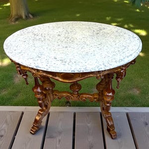 May include: A small, antique side table with a round, speckled white marble top. The table has ornate, dark brown wooden legs and a decorative apron. The table is approximately 28 inches in diameter.