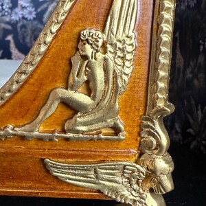 May include: A wooden bed frame with gold accents. The headboard features a carved angel with wings and a decorative scroll design. The footboard has a winged lion paw foot.