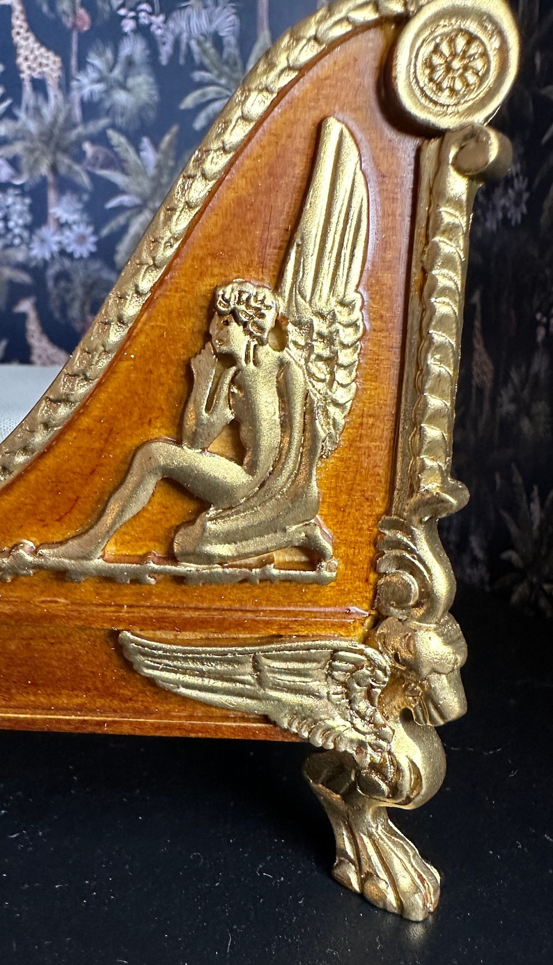 May include: A wooden bed frame with gold accents. The headboard features a carved angel with wings and a decorative scroll design. The footboard has a winged lion paw foot.