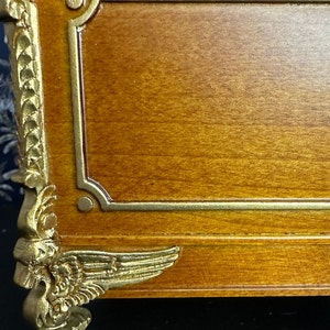 May include: A wooden box with gold accents and decorative feet. The box has a gold trim around the top and bottom edges. The feet are shaped like wings and have a gold finish.