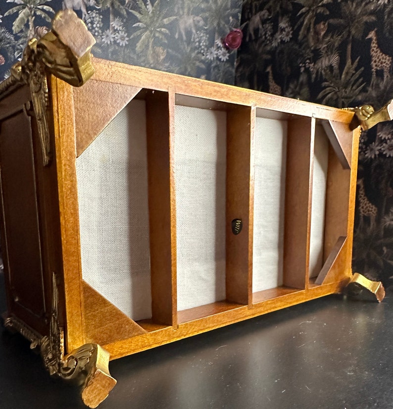 May include: A wooden display case with gold accents and a fabric-lined interior. The case has four compartments and is ideal for displaying small items.