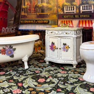 Puede incluir: Un juego de baño en miniatura con una bañera con patas de garra, un tocador y un inodoro. Los accesorios blancos están decorados con calcomanías florales. El fondo incluye un letrero del Moulin Rouge y una escena de la calle parisina.