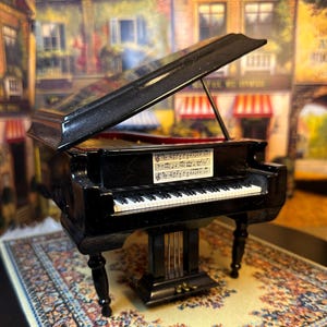 May include: A black miniature grand piano with a closed lid and a sheet of music on the music stand. The piano has a white and black keyboard and is sitting on a patterned rug.