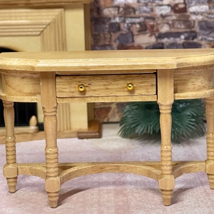 May include: A wooden console table with a single drawer and turned legs. The table has a light wood finish and gold-colored drawer pulls.