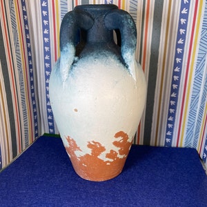 Op de afbeelding: Een kleine, witte keramische vaas met blauwe en bruine accenten. De vaas heeft twee handvatten en een rond lichaam.
