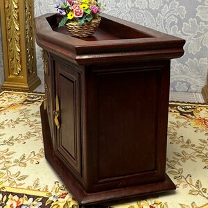 May include: A dark wood cabinet with a curved top and two doors. The cabinet has a decorative brass handle on each door. A basket of colorful flowers sits on top of the cabinet.