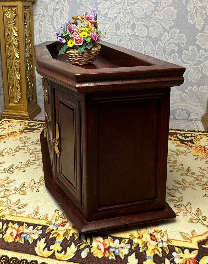 May include: A dark wood cabinet with a curved top and two doors. The cabinet has a decorative brass handle on each door. A basket of colorful flowers sits on top of the cabinet.