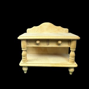 May include: A small, unfinished wooden cabinet with two drawers and a lower shelf. The cabinet has decorative turned legs and a scalloped top. The wood is a light, natural color, and the piece appears to be a miniature or dollhouse furniture item.
