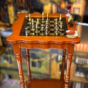 May include: A miniature wooden table with a chessboard set and a glass of wine. The chess pieces are gold and silver, and the board is black and white. The table has a scalloped edge and turned legs.