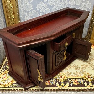 May include: A dark wood miniature cabinet with three drawers and two doors. The cabinet has a carved design on the front and brass handles. The cabinet is open and the drawers and doors are partially open.