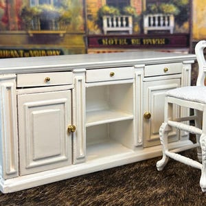 May include: White kitchen island with two doors, two drawers, and open shelves. The island is paired with a white wooden stool with a padded seat.
