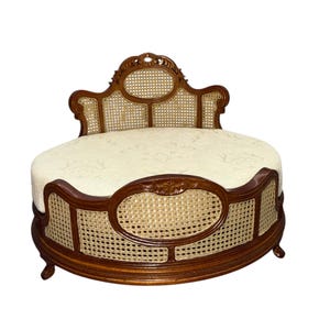 May include: A small, ornate, antique-style pet bed. The bed features a dark brown wooden frame with woven cane panels and a cream-colored, patterned cushion. The headboard is intricately carved.