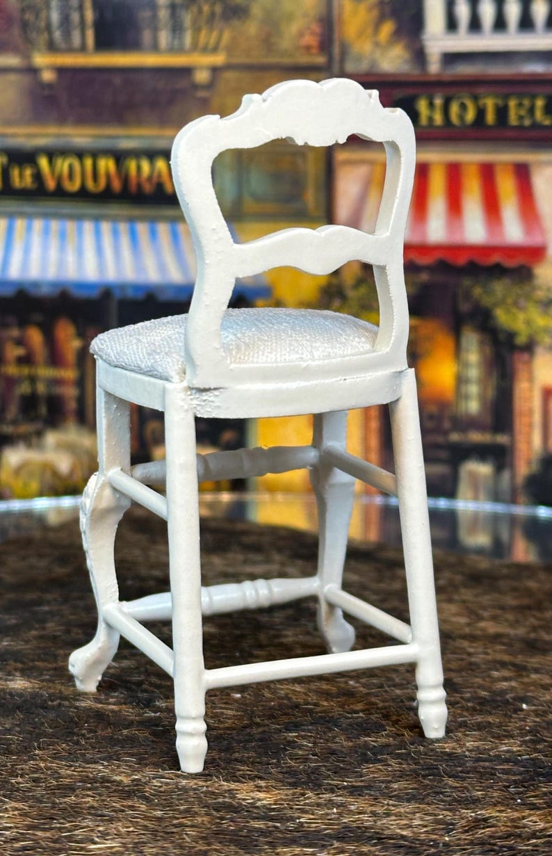 May include: White wooden bar stool with a padded seat and a decorative back. The stool has a simple design with a rectangular base and four legs.