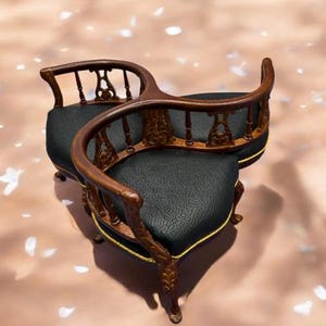 May include: A miniature, ornate wooden chair with a black leather seat and back. The chair has curved arms and a decorative backrest with intricate carvings. Gold trim accents the seat's edges.
