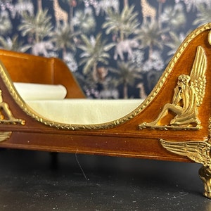 May include: A wooden chaise lounge with gold accents and winged cherub figures. The chaise has a white fabric cushion and sits on four gold feet.