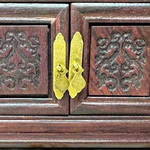 May include: A dark wood jewelry box with two doors and ornate carvings. The doors have brass handles and are closed.