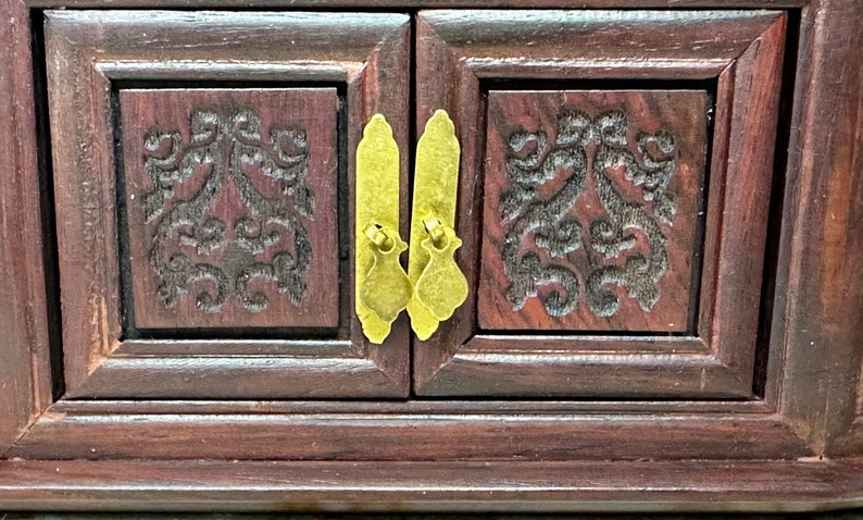 May include: A dark wood jewelry box with two doors and ornate carvings. The doors have brass handles and are closed.