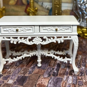 May include: White painted wooden console table with two drawers and ornate carved legs. The table has a distressed white finish and gold accents.