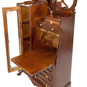 May include: Miniature wooden secretary desk with a dark brown finish. The desk features a drop-down writing surface, drawers with gold-colored knobs, and a glass-doored cabinet. The top has an ornate, arched design.