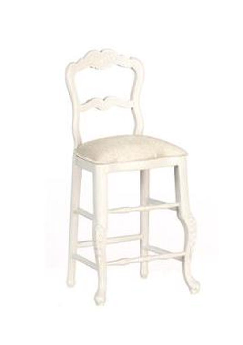 May include: White wooden bar stool with a carved back and legs. The stool has a beige upholstered seat.