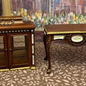 May include: Two miniature wooden furniture pieces, a cabinet with glass doors and a small table with ornate details. Both pieces feature a brown wood finish with gold accents and white porcelain inlays.