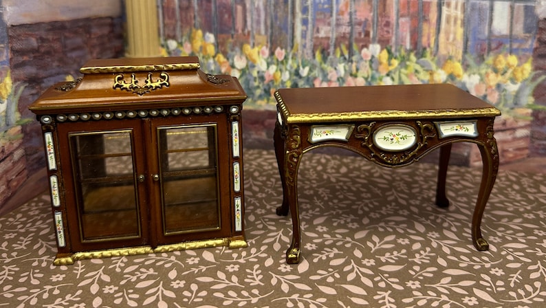 May include: Two miniature wooden furniture pieces, a cabinet with glass doors and a small table with ornate details. Both pieces feature a brown wood finish with gold accents and white porcelain inlays.