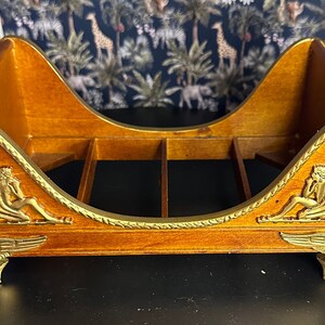 May include: A wooden decorative shelf with a gold finish. The shelf is shaped like a chaise lounge with winged cherubs on each side. The shelf has a gold rope design around the edge.