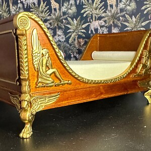May include: A wooden chaise lounge with gold accents and intricate carvings. The chaise has a white fabric cushion and ornate legs.