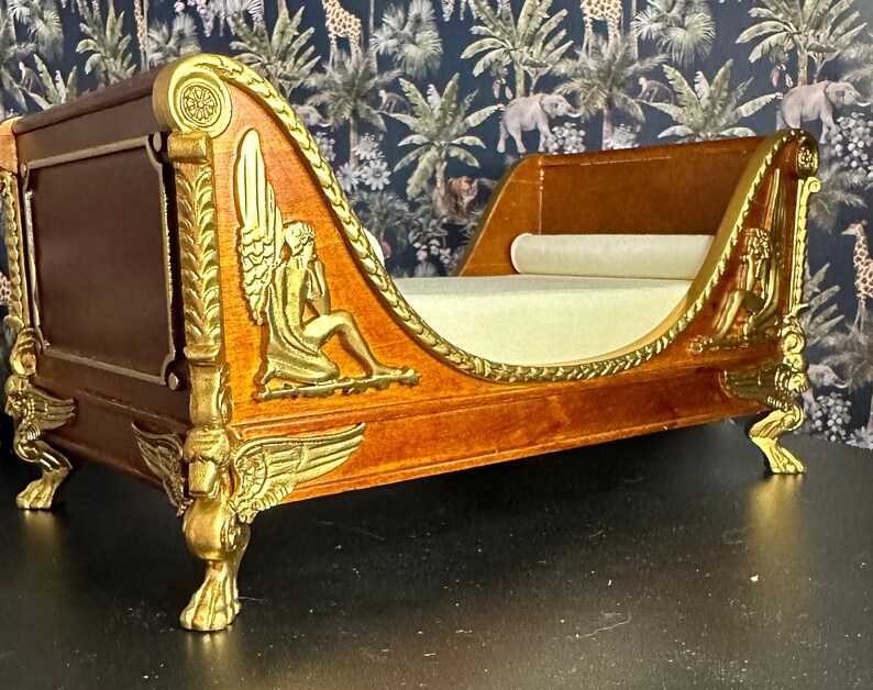 May include: A wooden chaise lounge with gold accents and intricate carvings. The chaise has a white fabric cushion and ornate legs.