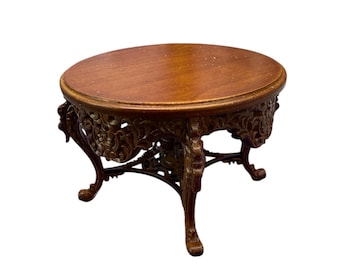 May include: A small, antique-style wooden table with an oval top and ornate, carved legs. The table is brown with a dark finish, and the legs have a detailed, floral design. The table is approximately 18 inches in diameter and 16 inches tall.