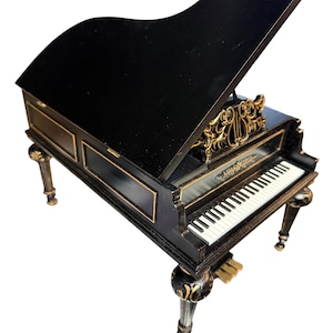 May include: A miniature black grand piano with gold accents. The piano has a glossy finish, a hinged lid, and a keyboard with white and black keys. The legs are ornate, and the design includes gold filigree details. A decorative musical instrument.