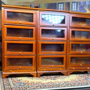 May include: A set of three wooden bookcases with glass doors and shelves. The bookcases are a rich brown color and have a traditional design.